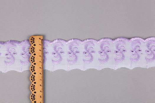 straight strip of purple white cotton ribbon with embroidery and wooden ruler on gray background. National pattern for sewing. pattern and interweaving threads. texture for websites. Space for text.