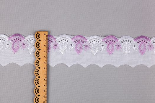 straight strip of purple white cotton ribbon with embroidery and wooden ruler on gray background. National pattern for sewing. pattern and interweaving threads. texture for websites. Space for text.