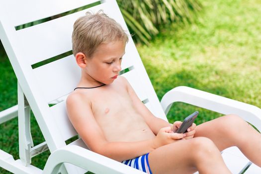 Boy playing games on the telephone. Gadget dependency disorder problem for kids during holiday vacation at the seaside concept
