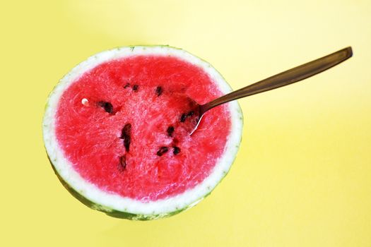 half watermelon with a spoon on a yellow background, copy space