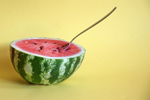 half watermelon with a spoon on a yellow background, copy space