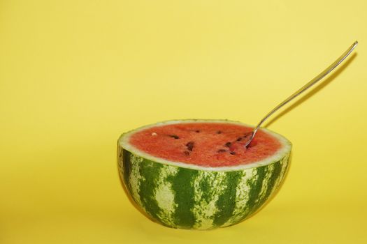 half watermelon with a spoon on a yellow background, copy space