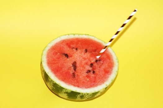 half watermelon with cocktail straw on yellow background, copy space.