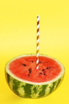 half watermelon with cocktail straw on yellow background, close-up