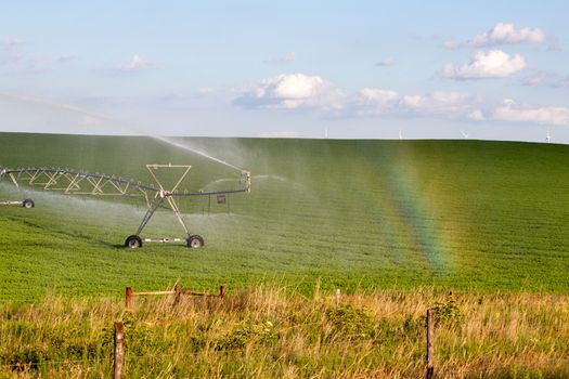 Pivot running in field with rainbow on sunny day . High quality photo