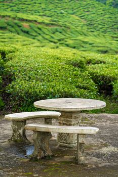 A place for relaxation and tea drinking made of stone furniture overlooking a green valley of tea bushes