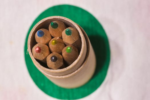 Colored pencils inserted in a cardboard cylinder on a colored plane, horizontal image