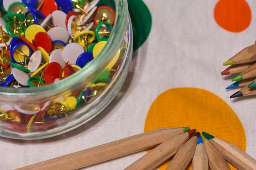 colored thumbtacks in a glass jar and colored pencils