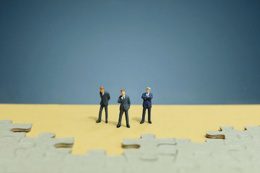 Business strategy conceptual photo - Group of miniature businessman standing on wooden table in front of missing piece puzzle