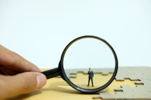 Business strategy conceptual photo - Miniature businessman standing behind magnifier glass in the middle of jigsaw puzzle