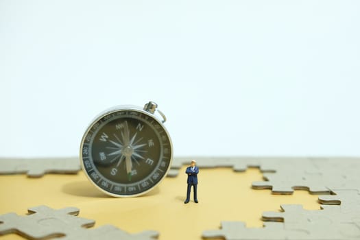 Business strategy conceptual photo - Miniature businessman standing beside compass in the middle of jigsaw puzzle