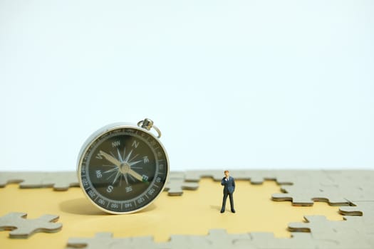 Business strategy conceptual photo - Miniature businessman thinking beside compass in the middle of jigsaw puzzle