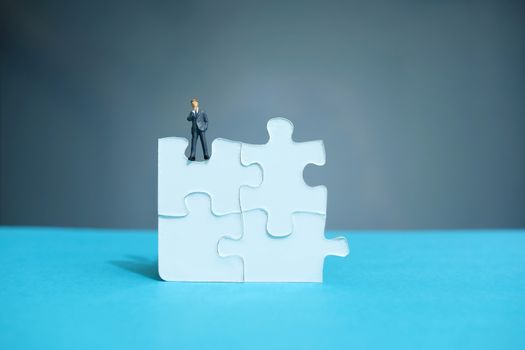 Conceptual photo of business strategy – miniature people standing on four joined jigsaw puzzle