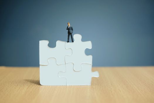 Conceptual photo of business strategy – miniature people standing on four joined jigsaw puzzle