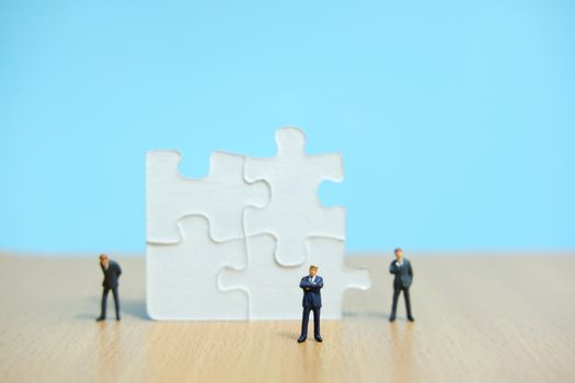 Business strategy conceptual photo - Group of miniature businessman standing on wooden table in front of missing piece puzzle