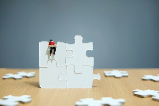 Conceptual photos of business strategies - Miniature businessmen seat above 4 jigsaw puzzles that are arranged