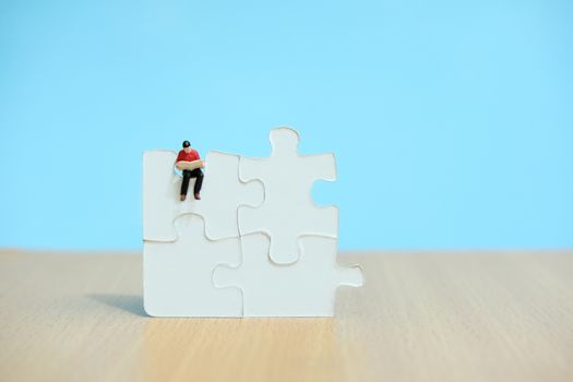 Conceptual photos of business strategies - Miniature businessmen seat above 4 jigsaw puzzles that are arranged