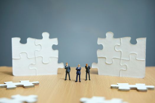 Business strategy conceptual photo - Group of miniature businessman standing on wooden table in front of missing piece puzzle