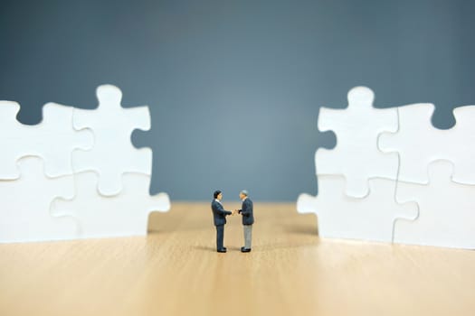 Business strategy conceptual photo - Miniature businessman make handshake partnership in the center of jigsaw puzzle piece that are arranged