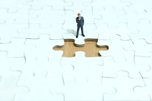 Business strategy conceptual photo - Miniature businessman thinking in front of missing piece puzzle