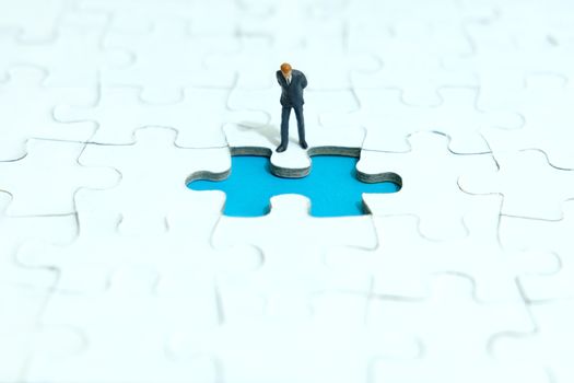 Business strategy conceptual photo - Miniature businessman looking down at missing piece puzzle