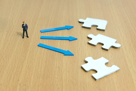 Business strategy conceptual photo - Miniature businessman thinking to choose alternative between three puzzle piece