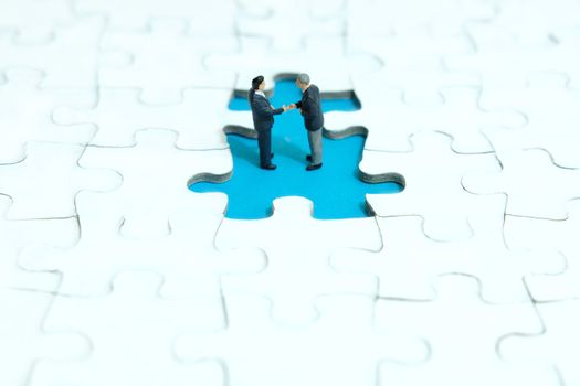 Business strategy conceptual photo - two miniature businessman make handshake partnership agreement inside missing piece of puzzle