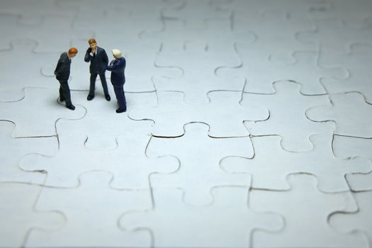 Business strategy conceptual photo - three miniature businessman discussion above puzzle jigsaw