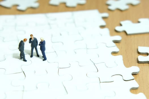 Business strategy conceptual photo - Group of miniature businessman have a discuss above puzzle jigsaw