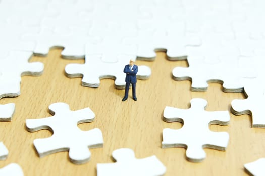 Business strategy conceptual photo - Miniature businessman standing in the center of jigsaw puzzle piece