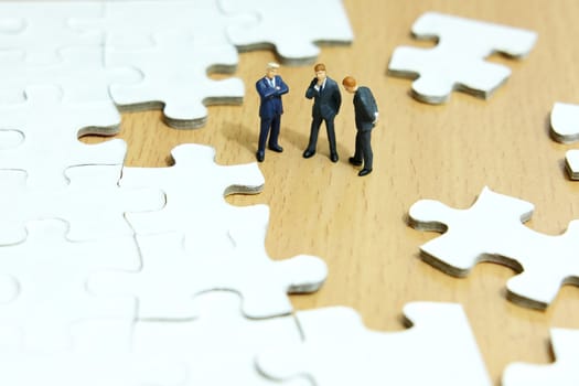 Business strategy conceptual photo - Group of miniature businessman have a discuss above puzzle jigsaw