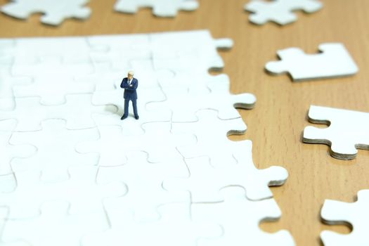 Business strategy conceptual photo - Miniature businessman standing above puzzle jigsaw