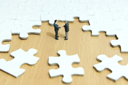 Business strategy conceptual photo - Miniature businessman make handshake partnership in the center of jigsaw puzzle piece