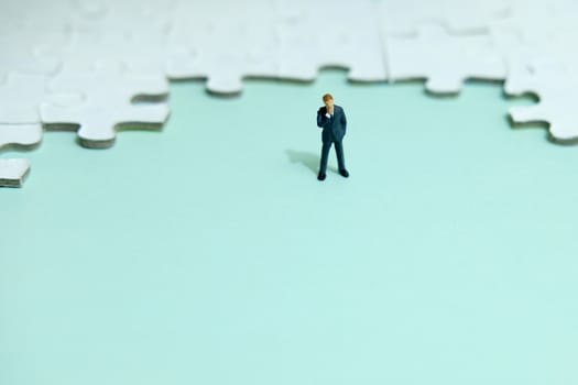 Business strategy conceptual photo - Miniature businessman thinking in front of puzzle jigsaw