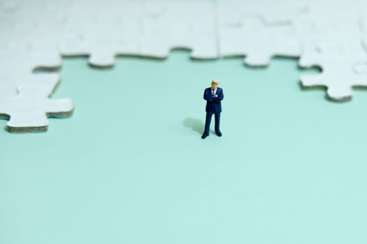 Business strategy conceptual photo - Miniature businessman standing in front of puzzle jigsaw