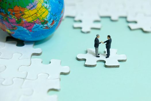 Business strategy conceptual photo - Miniature businessman make handshake partnership above jigsaw puzzle piece with globe