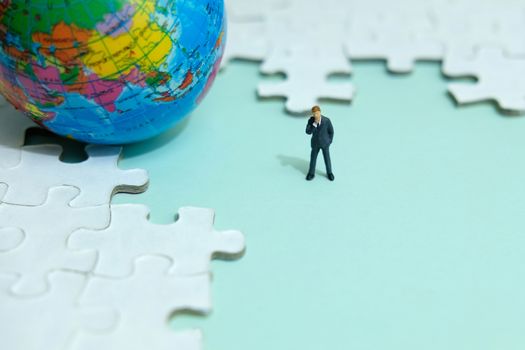 Business strategy conceptual photo - Miniature businessman standing in the middle of jigsaw puzzle with globe