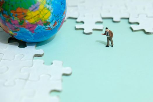 Business strategy conceptual photo - Miniature businessman pointing on empty jigsaw puzzle space with globe