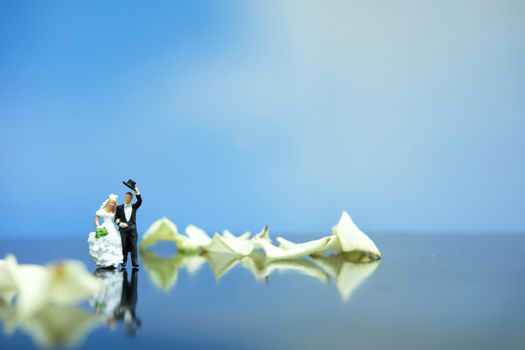 Miniature photography outdoor marriage wedding concept, bride and groom walking on white rose flower pile