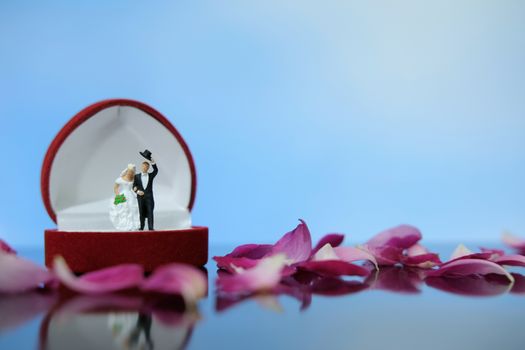 Miniature photography outdoor marriage wedding concept, bride and groom standing above opened ring box on red white rose flower pile