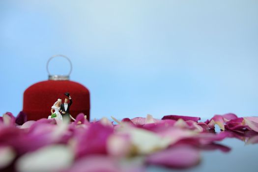 Miniature photography outdoor marriage wedding concept, bride and groom walking in front of opened ring box on red white rose flower pile