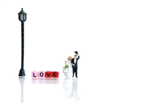 Miniature people photography. Bride and groom with love word beads on shiny white background