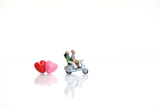 Miniature people photography for valentines day, young couple riding scooter with heart beads on shiny white background