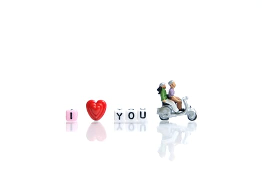 Miniature people photography for valentines day, young couple riding scooter with I love you beads on shiny white background