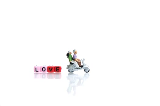 Miniature people photography for valentines day, young couple riding scooter with heart shape and love beads on shiny white background