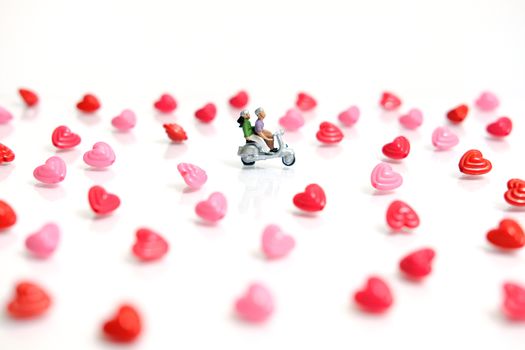 Miniature people photography for valentines day, young couple riding scooter with I love you beads on shiny white background