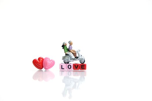 Miniature people photography for valentines day, young couple riding scooter with I love you beads on shiny white background