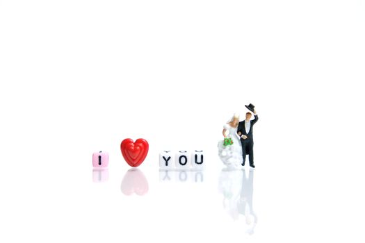 Miniature people photography for valentines day, bride and groom with heart shape and I love you word beads on shiny white background