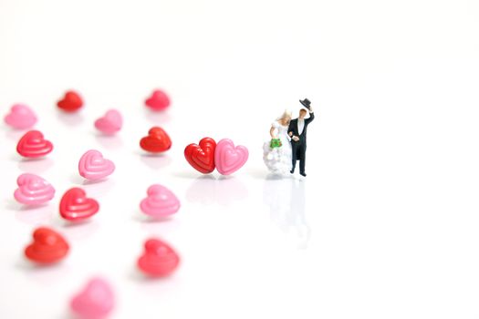 Miniature people photography for valentines day, bride and groom with heart shape and love word beads on shiny white background