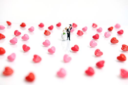 Miniature people photography. Bride and groom with heart shape and love word beads on shiny white background